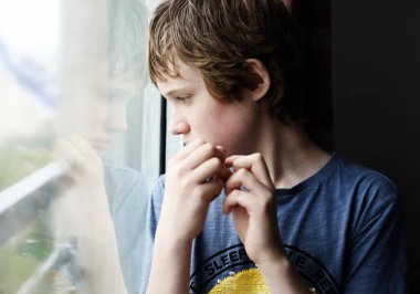 Pencereden içeri bakan 12 yaşında tatlı bir otistik çocuk.