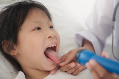 Hastanede küçük kız ağzını muayene eden kadın doktor genç bir hastanın boğazını kontrol ediyor.