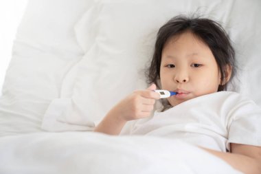 Ağzı termometreyle yatakta yatan hasta kız.