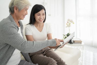 Annesiyle kızı evde dijital tablet kullanıyorlarmış. Gülümseyen aile ekrana bakıyor, online alışveriş yapıyor.