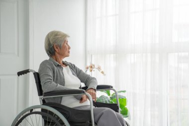 Tekerlekli sandalyede oturan yaşlı bir kadının pencereden dışarı bakışı. Hastane odasındaki yaşlı kadın pencerenin yanında oturup düşünüyor. Yaşlı hasta hastanede üzgün ve yalnız hissediyor..