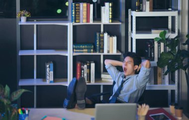 Taylandlı rahat genç iş adamı ofiste bacaklarıyla uyur gece geç saatlere kadar masa başında uyur.