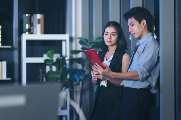 Businesspeople in the office at night working late, Two young businesspeople working overtime together over a laptop at a desk in an office in the late evening