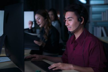 Taylandlı Asyalı müşteri hizmetleri operatörleri çağrı merkezinde gece vardiyasında çalışıyorlar. Gece iş yerinde müşterilerine yardım ediyorlar.