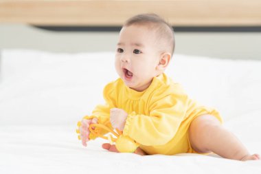 Yeni doğan tatlı Taylandlı bebek yatakta komik oynuyor. Bebek bezli küçük bebek beyaz yatakta oyuncaklarla yatıyor.