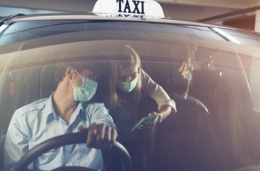 Yeni normal. Maskeli bir arabanın arkasında oturan bir ergen. Taksideki genç bir kadın maskeyle korunuyor. Yol güvenliği. Koronavirüs salgını. akıllı telefon kullan rota seyahati bul