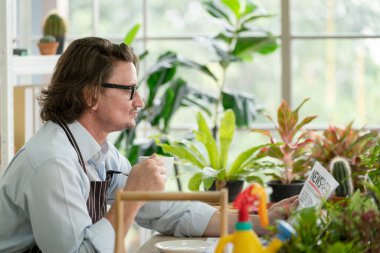 Modern yeşil bahçe evinde gazete okurken gözlüklü bir adam oturmuş kahvesini yudumluyor.