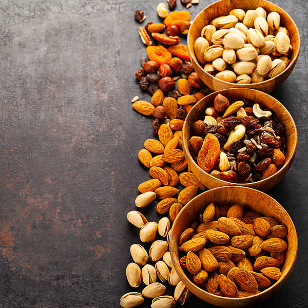 mix of different nuts and dried fruits in wooden bowls standing on rustic background