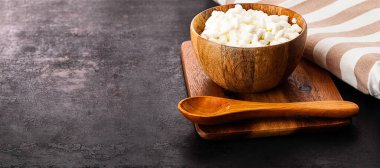 Ahşap tahtada duran süzme peynirli ve kaşıklı ahşap kase. Eski kırsal arka planda duruyor