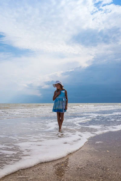 Prachtige zeegezicht. Meisje in jurk en witte hoed op het strand over blauwe hemel achtergrond Rechtenvrije Stockfoto's