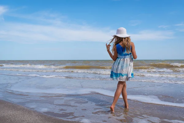 Smuk pige i hvid hat og farverig kjole på stranden over blå himmel baggrund - Stock-foto