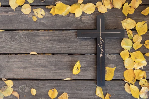 Herfst achtergrond. Van hout zwart kruis op armoedig donker houten bord met gele bladeren Rechtenvrije Stockafbeeldingen