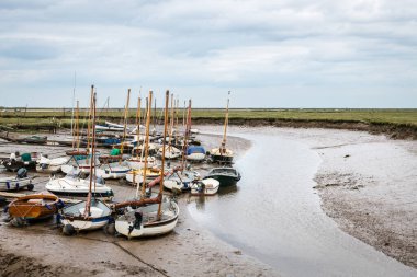 Small sail boats moored at Blakeney Harbour in Norfolk during low tide on a cloudy Summer day. clipart