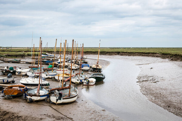 Small sail boats moored at Blakeney Harbour in Norfolk during low tide on a cloudy Summer day.