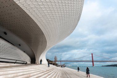 LISBON - 4 Ocak 2018: Lizbon 'daki Tagus Nehri' nin kıyısındaki Sanat, Mimarlık ve Teknoloji Müzesi 'nin (MAAT) merdivenleri boyunca yürüyen ve arka planında 25 Nisan Köprüsü bulunan insanlar.