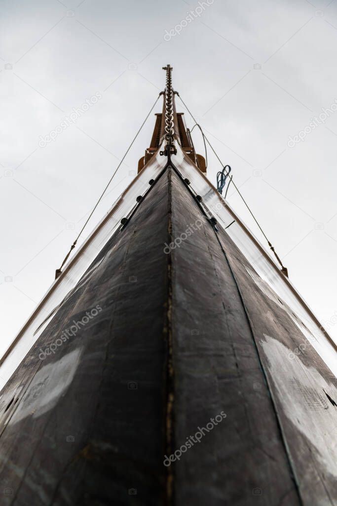 Low angle-view of the bow of a wooden luxury sail boat against a cloudy sky.