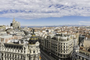 Gran Va ve Madrids 'in gökyüzü manzarası bir yaz sabahı erken saatlerde yükselirken, Metropolis binası ön planda tanınacaktır. Faro de Moncloa 'daki Telefon Binası gibi bazı başka simgeler de tanınacak..