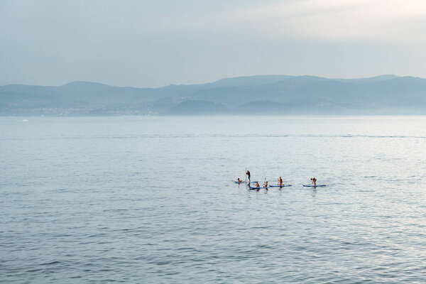 PORTONOVO, SPAIN - AUGUST 11, 2020: A group of young people enjoy practising paddle surf in the Ria de Pontevedra on a foggy Summer day.