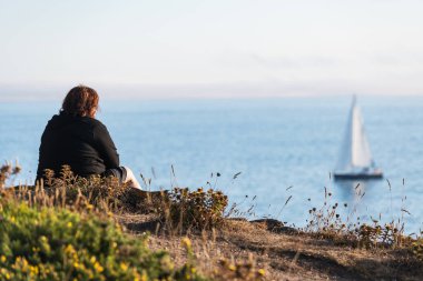 Yalnız, orta yaşlı bir kadın, gün batımında Galiçya 'daki Ria de Pontevedra' da Ons Adası 'ndan giden bir tekneyi seyrediyor..