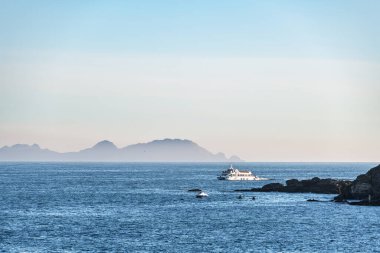 Günbatımında Galiçya 'da Ria de Pontevedra' da yalnız bir feribot dolaşır ve arka planda Cies Adaları bulunur..