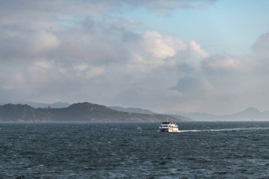 Günbatımında Galiçya 'da Ria de Pontevedra' da yalnız bir feribot dolaşır ve arka planda Cies Adaları bulunur..
