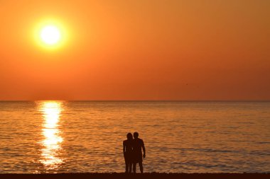 Gün doğumunda sahilde romantik sarılma çift siluetleri
