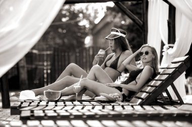 Mayolu iki güzel kız, ellerinde meyve tabağıyla odunların önünde poz veriyorlar.