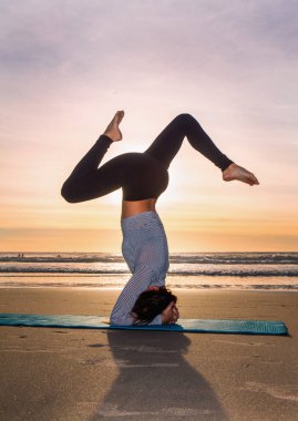 Gün batımında plajda yoga yapan bir kadın.