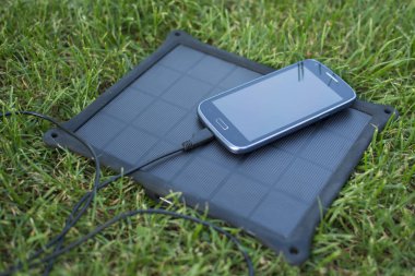 Yenilenebilir enerji - güneş ile doğada çimenlerin üzerinde cep telefonu şarj kullanımı