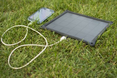 Yenilenebilir enerji - güneş ile doğada çimenlerin üzerinde cep telefonu şarj kullanımı