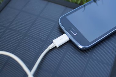 Yenilenebilir enerji - güneş ile doğada çimenlerin üzerinde cep telefonu şarj kullanımı