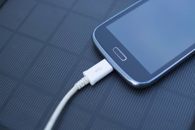 Yenilenebilir enerji - güneş ile doğada çimenlerin üzerinde cep telefonu şarj kullanımı