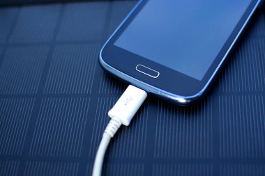 Yenilenebilir enerji - güneş ile doğada çimenlerin üzerinde cep telefonu şarj kullanımı