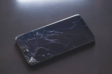Siyah masaüstünde kırık dokunmatik ekranlı akıllı telefon