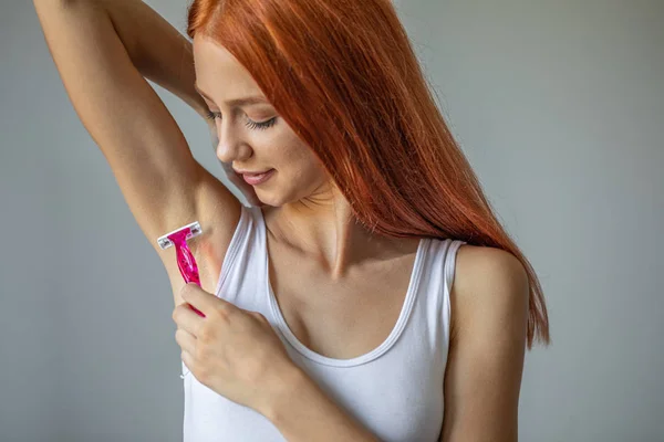 Улыбающаяся женщина бреет подмышки розовой бритвой — стоковое фото