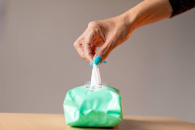 Turkuaz tırnaklı yaşlı bir kadın cildini temizlemek için ıslak mendil kullanıyor.