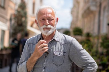 Sokakta sakallı mutlu yaşlı adam poz veriyor ve gülümsüyor, portre, bulanık sokak geçmişi