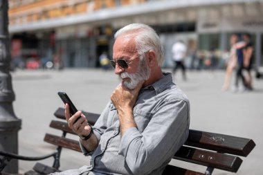 Yaşlı adam akıllı telefonlarda internet uygulaması kullanıyor, şehir içi stok fotoğrafı.