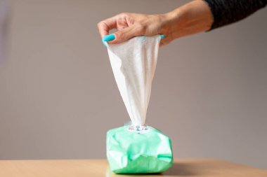 Turkuaz tırnaklı yaşlı bir kadın cildini temizlemek için ıslak mendil kullanıyor.