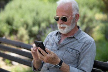 Yaşlı adam akıllı telefon, açık hava, park uygulamasında geziniyor.