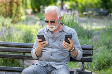 Yaşlı adam iki akıllı telefonu karşılaştırıyor.