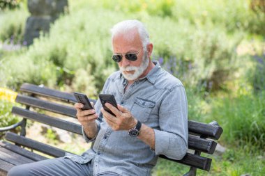 Yaşlı adam iki akıllı telefonu karşılaştırıyor.
