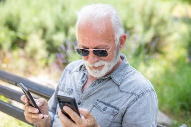 Yaşlı adam iki akıllı telefonu karşılaştırıyor.