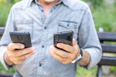 Yaşlı adam iki akıllı telefonu karşılaştırıyor.