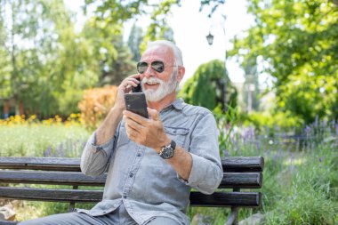 Yaşlı adam iki akıllı telefonu karşılaştırıyor.