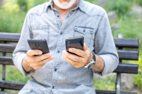 Yaşlı Adam Iki Akıllı Telefonu Karşılaştırıyor — Stok fotoğraf