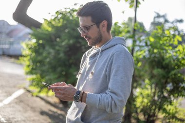 Akıllı görünümlü bir adam akıllı telefondan mesaj yolluyor, açık hava parkı çekimi, arka ışık.