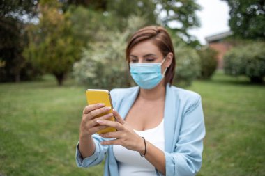 Mavi maskeli bir kadın, açık hava fotoğrafı kullanıyor.