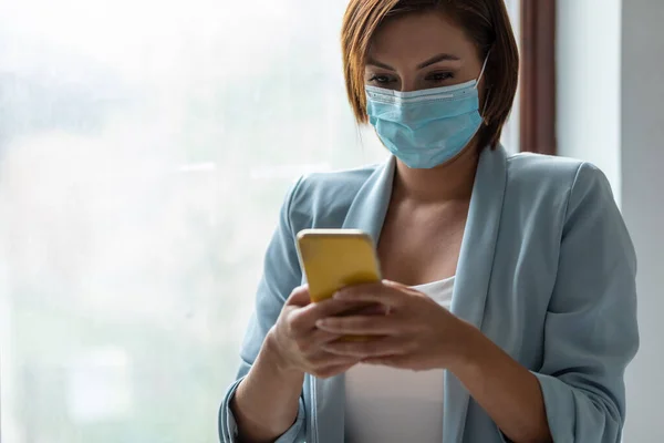 Donna Con Maschera Facciale Utilizzando Smartphone Indoor — Foto Stock