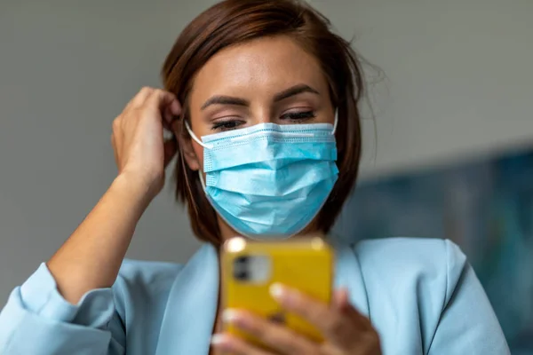 Woman with face mask using smartphone indoor